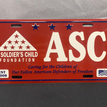 Decorative license plate - red background with white logo and letters, and the mission in blue text.